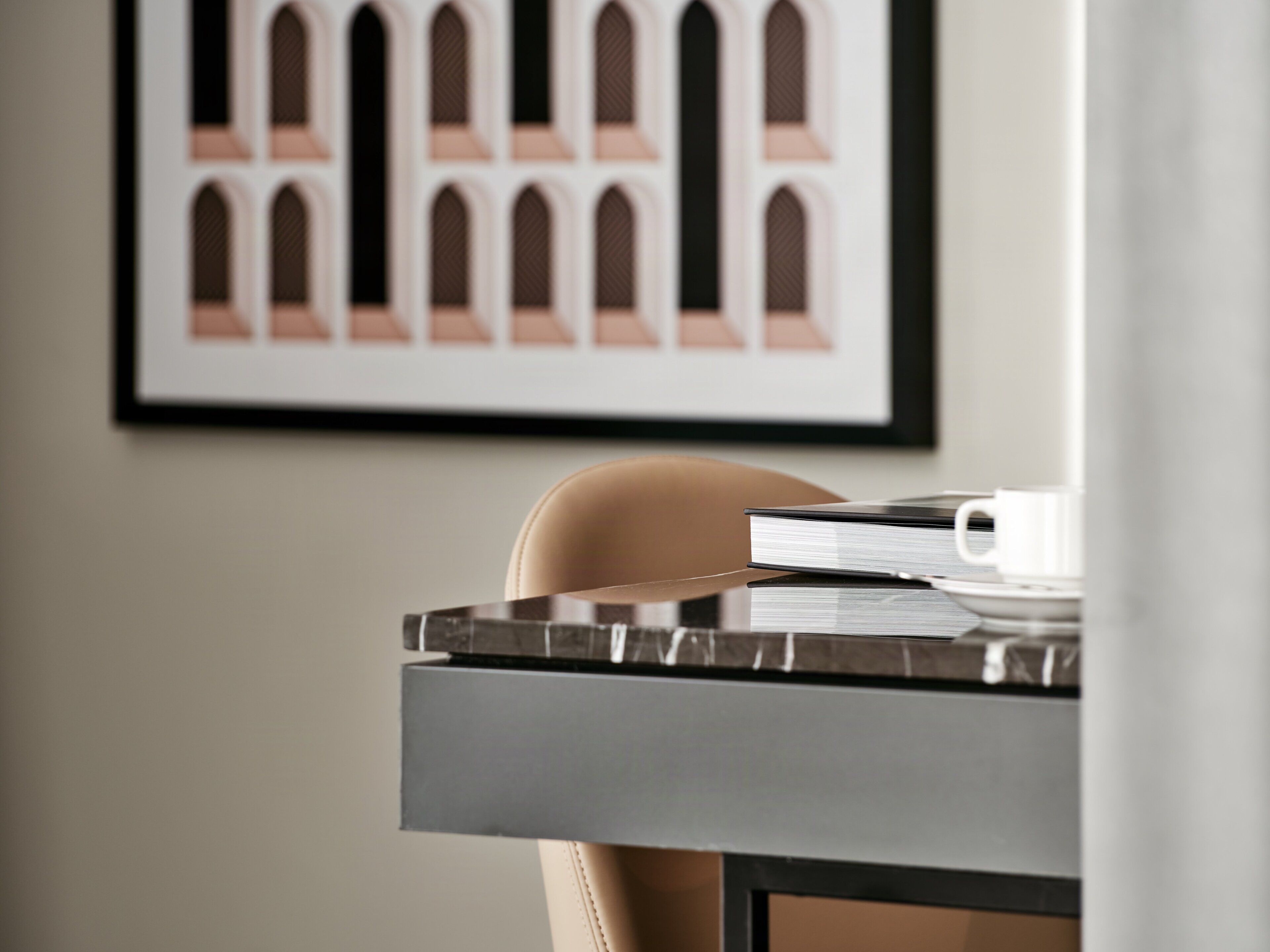 A framed architectural drawing on the wall, a table with a book and a cup, and a chair.