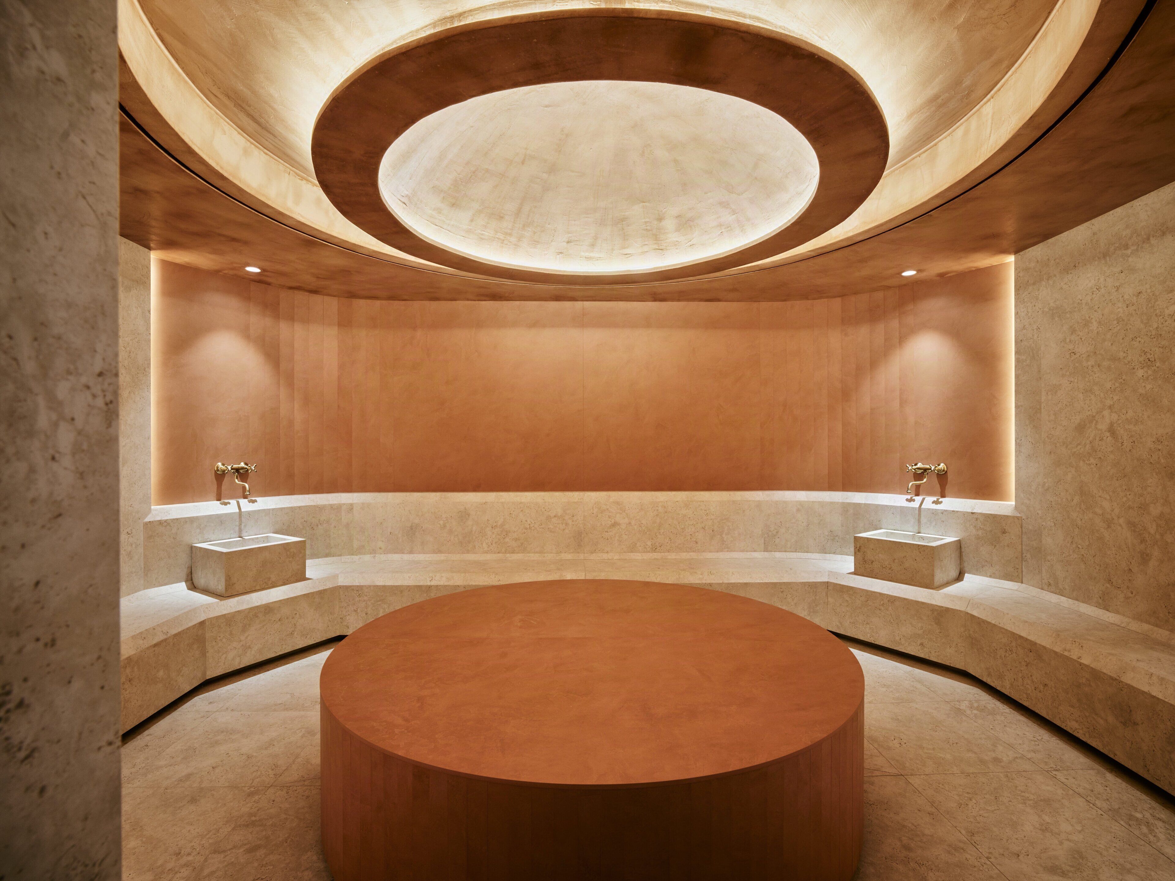 A circular room with a central round table, two sinks, and a recessed ceiling.