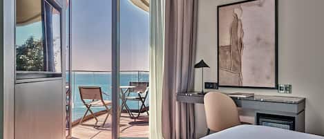 Habitación de hotel con cama, escritorio, silla, lámpara y un amplio ventanal con vista al océano.