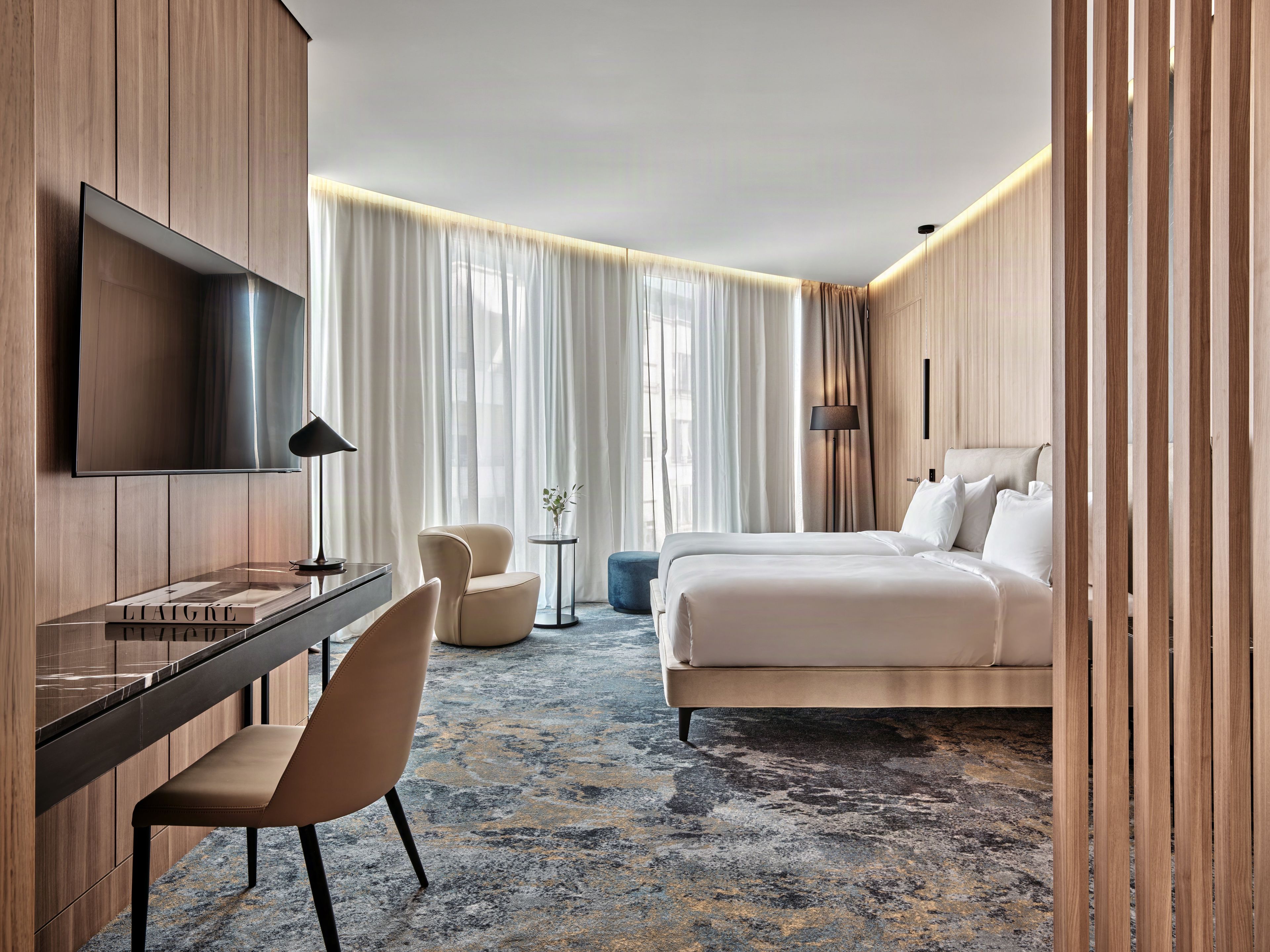 Een hotelkamer met een bed, een bureau, een stoel, een televisie en een groot raam met gordijnen.