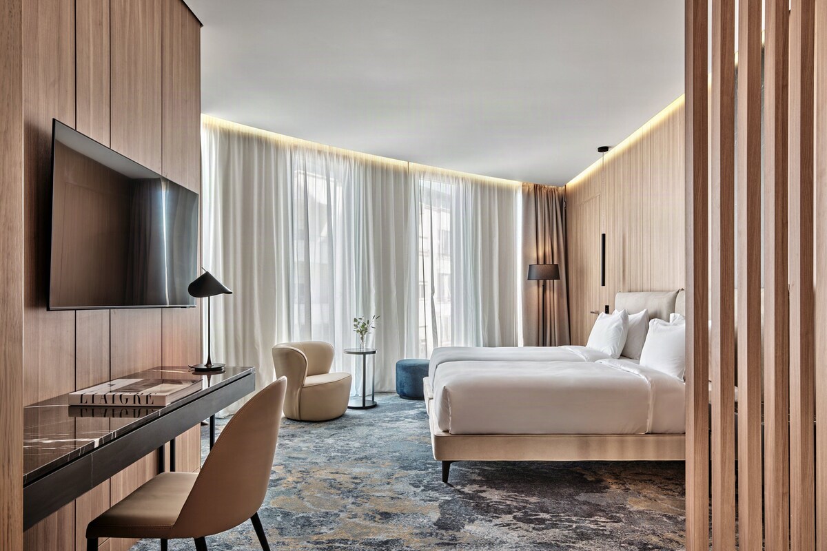 Une chambre d’hôtel équipée d’un lit, d’un bureau, d’une chaise, d’une télévision et d’une grande fenêtre avec des rideaux.