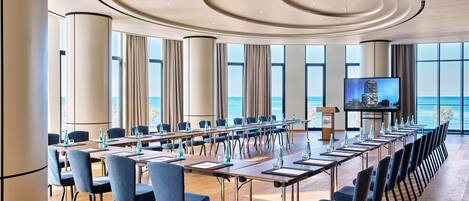A conference room with a long table, chairs, a podium, and a TV screen.