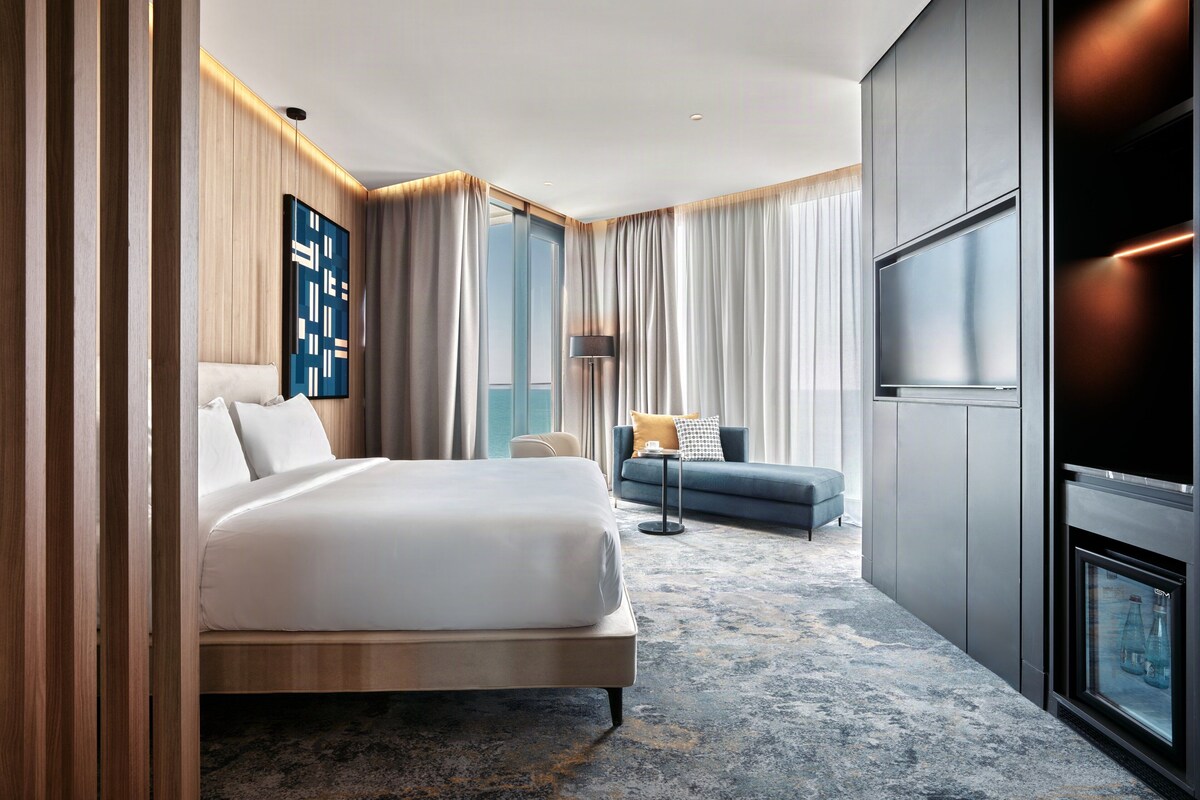 Une chambre d’hôtel moderne dotée d’un grand lit, d’un canapé, d’une télévision et offrant une vue sur la ville.