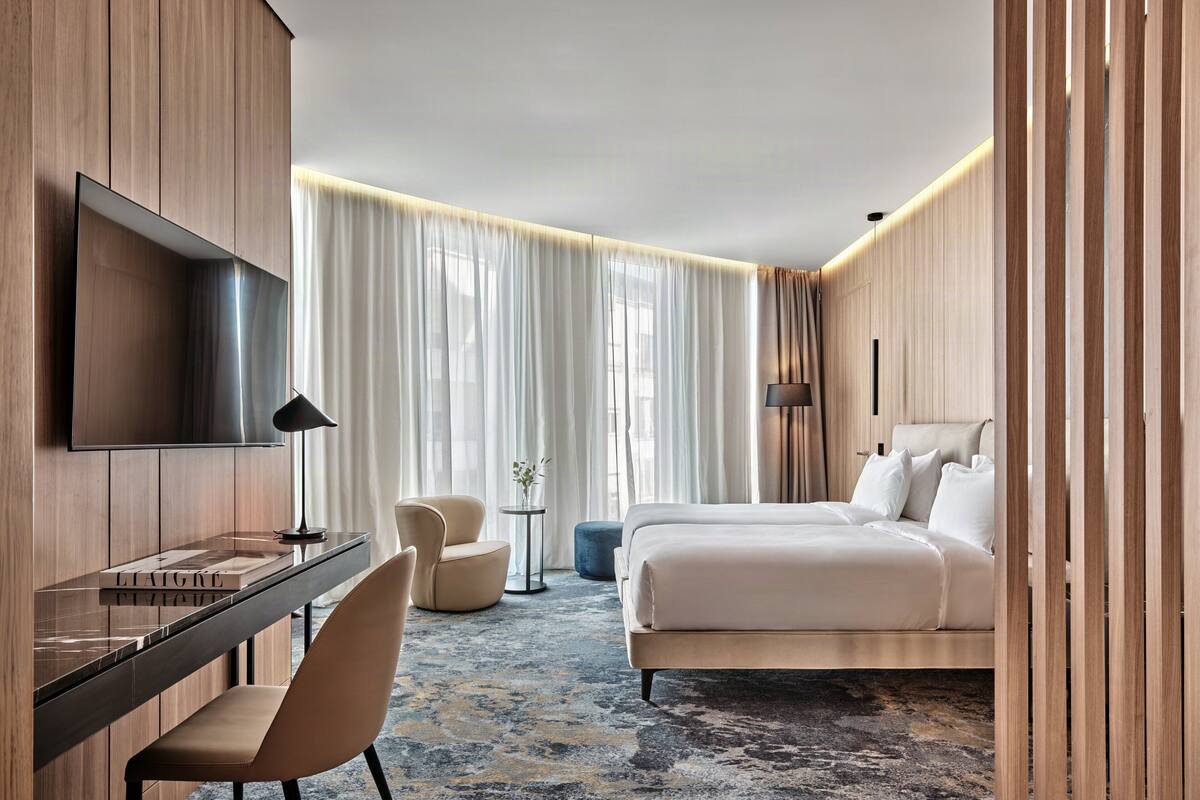 Ein Hotelzimmer mit Bett, Schreibtisch, Stuhl, Fernseher und einem großen Fenster mit Vorhängen.