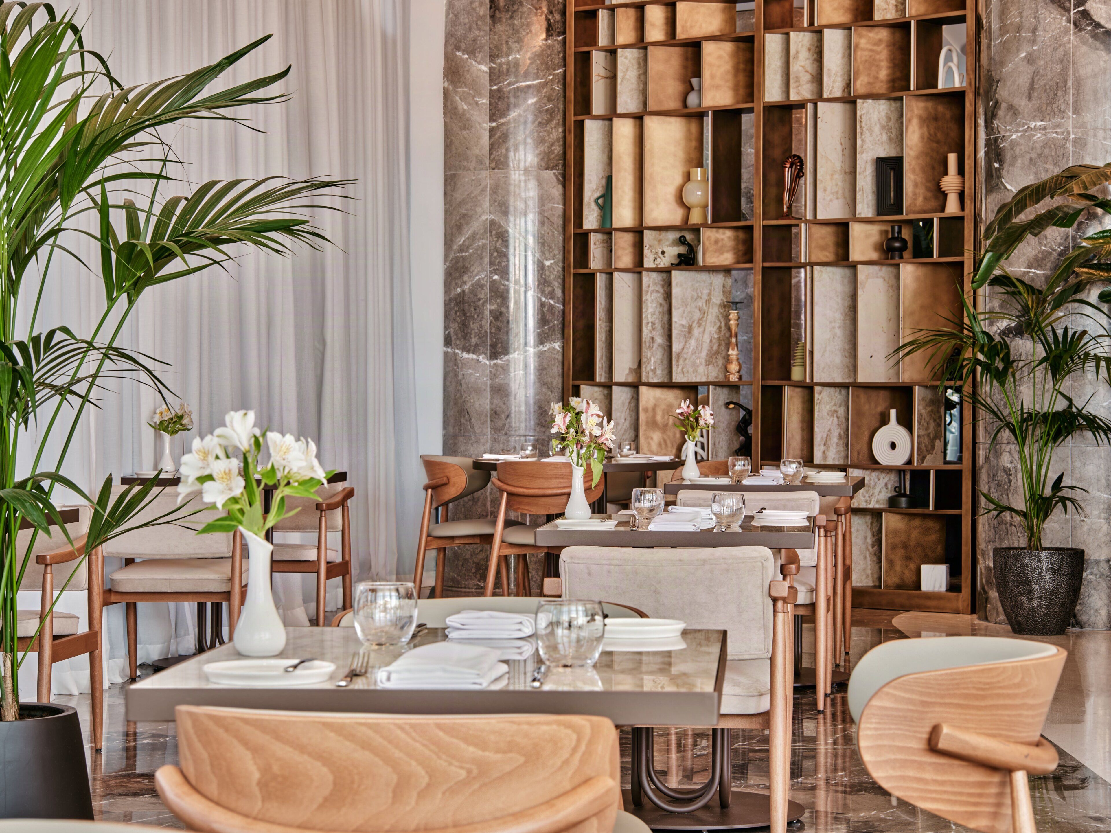 A dining area with wooden chairs, a marble table, and a bookshelf filled with various items.