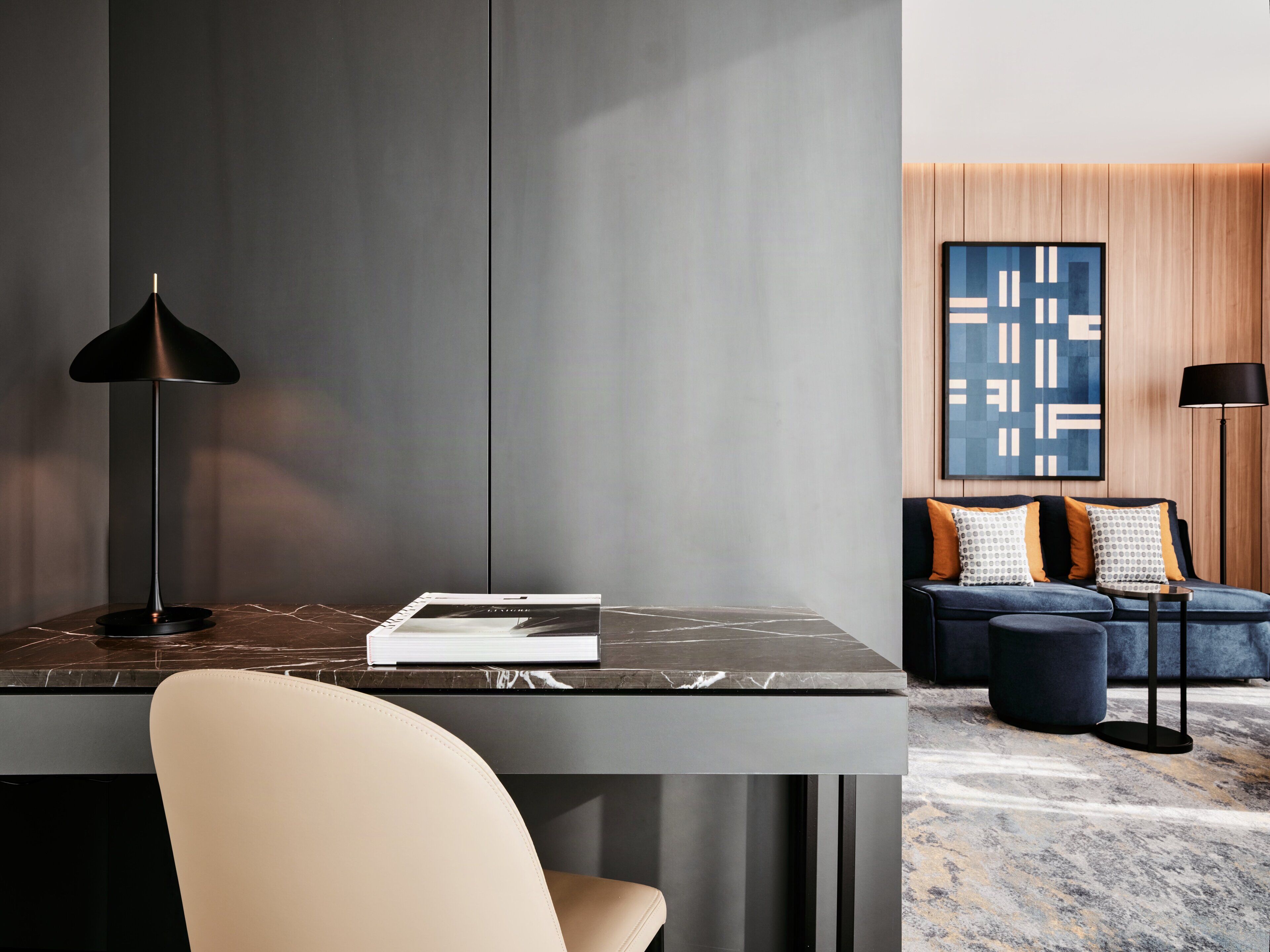 Een moderne kamer met een marmeren bureau, een zwarte lamp, een bank met gestreepte kussens en een blauw abstract schilderij aan de muur.