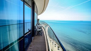Un balcon avec vue sur la mer, un mur en verre et une table avec des chaises.