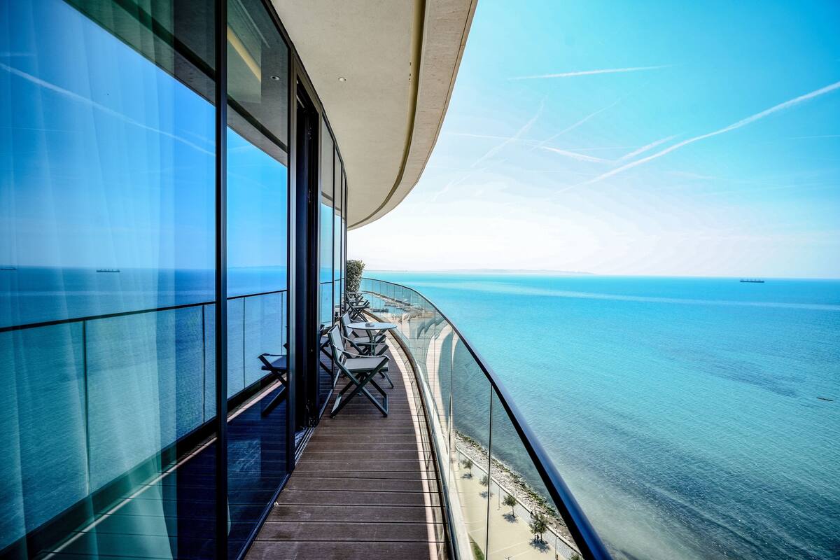 Een balkon met uitzicht op zee, een glazen wand en een tafel met stoelen.