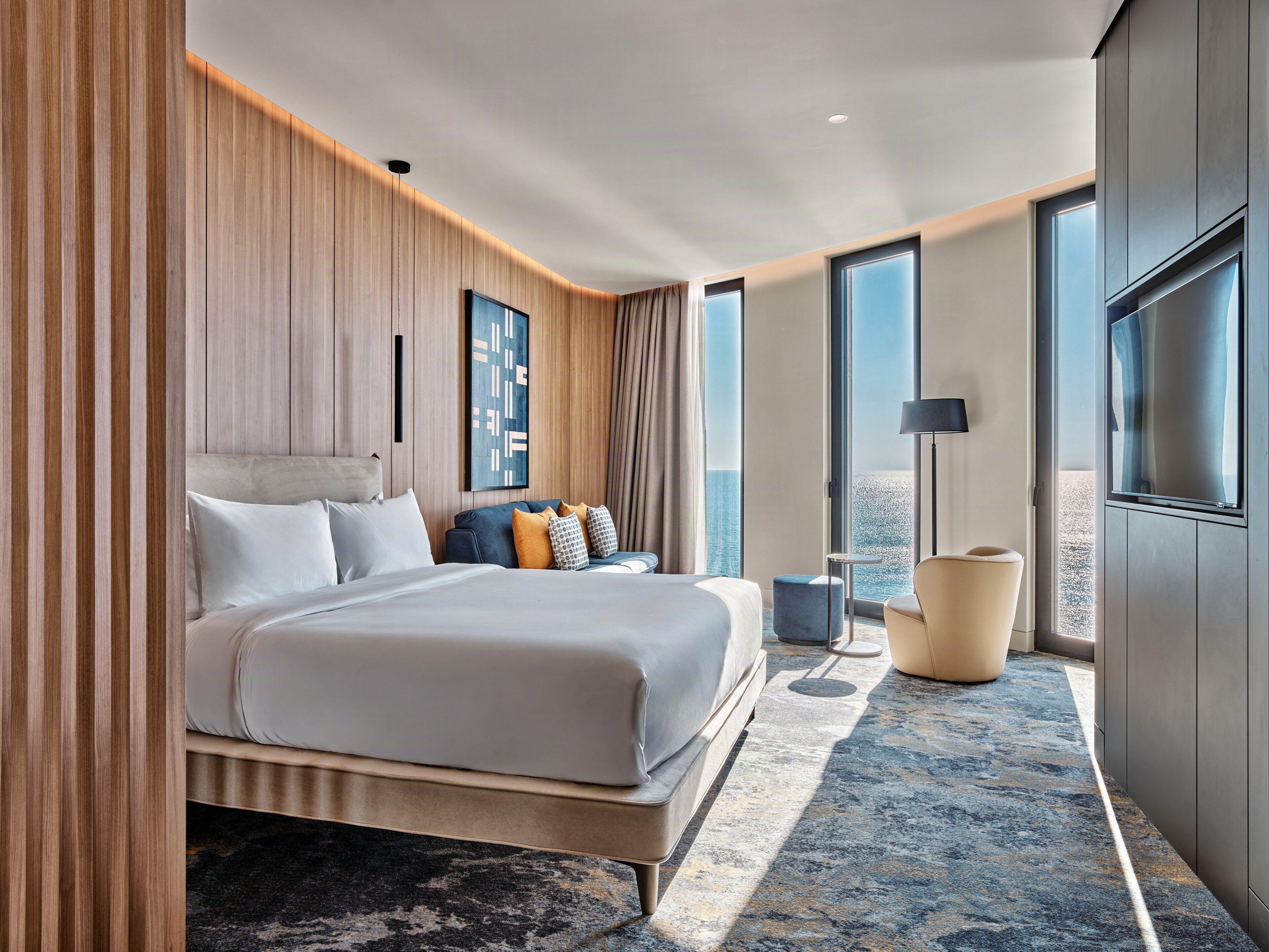 A modern hotel room with a large bed, a seating area, and a view of the ocean.