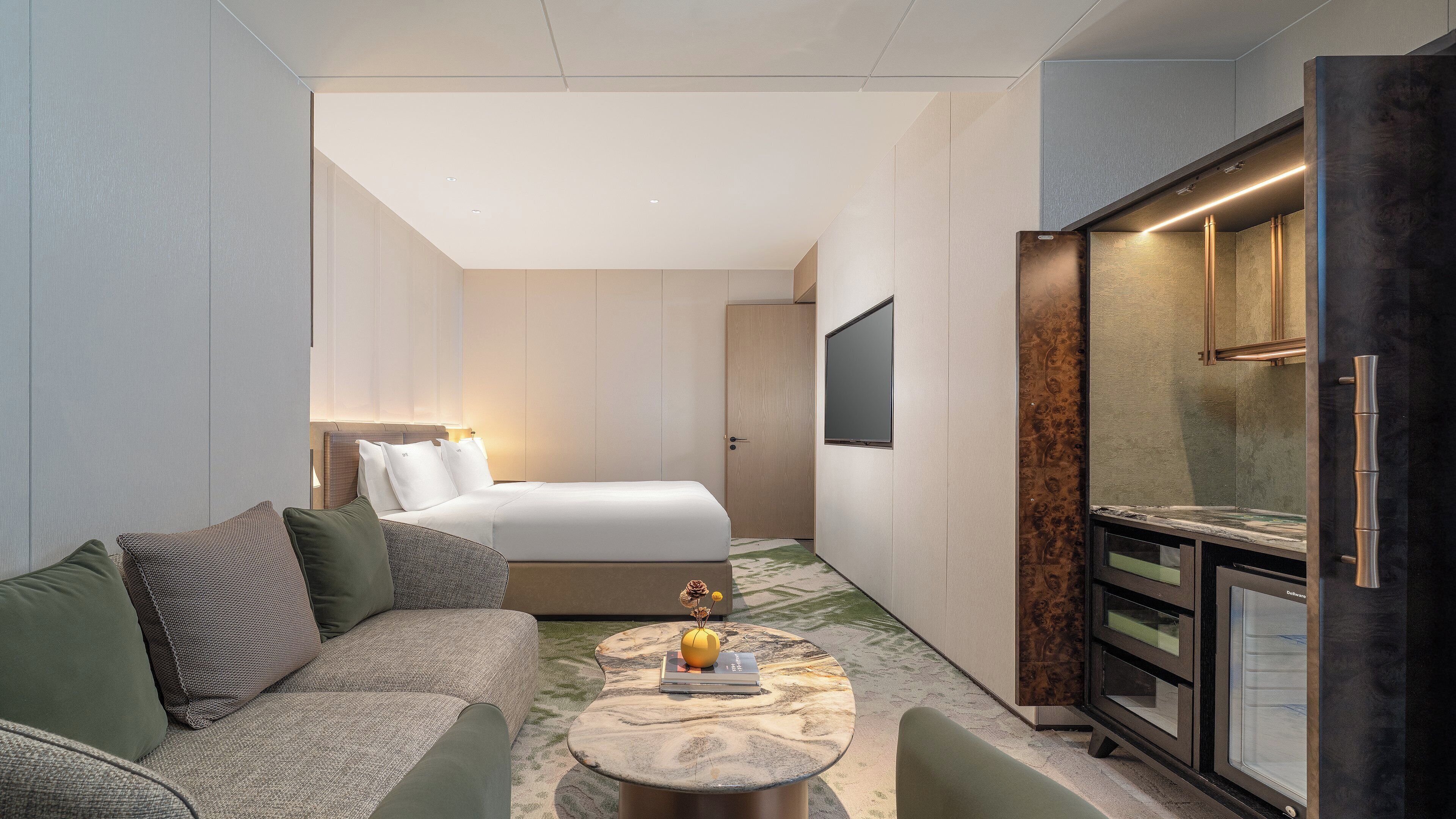 Ein Hotelzimmer mit Bett, Sofa, einem kleinen Tisch mit einer Vase und einer Minibar.