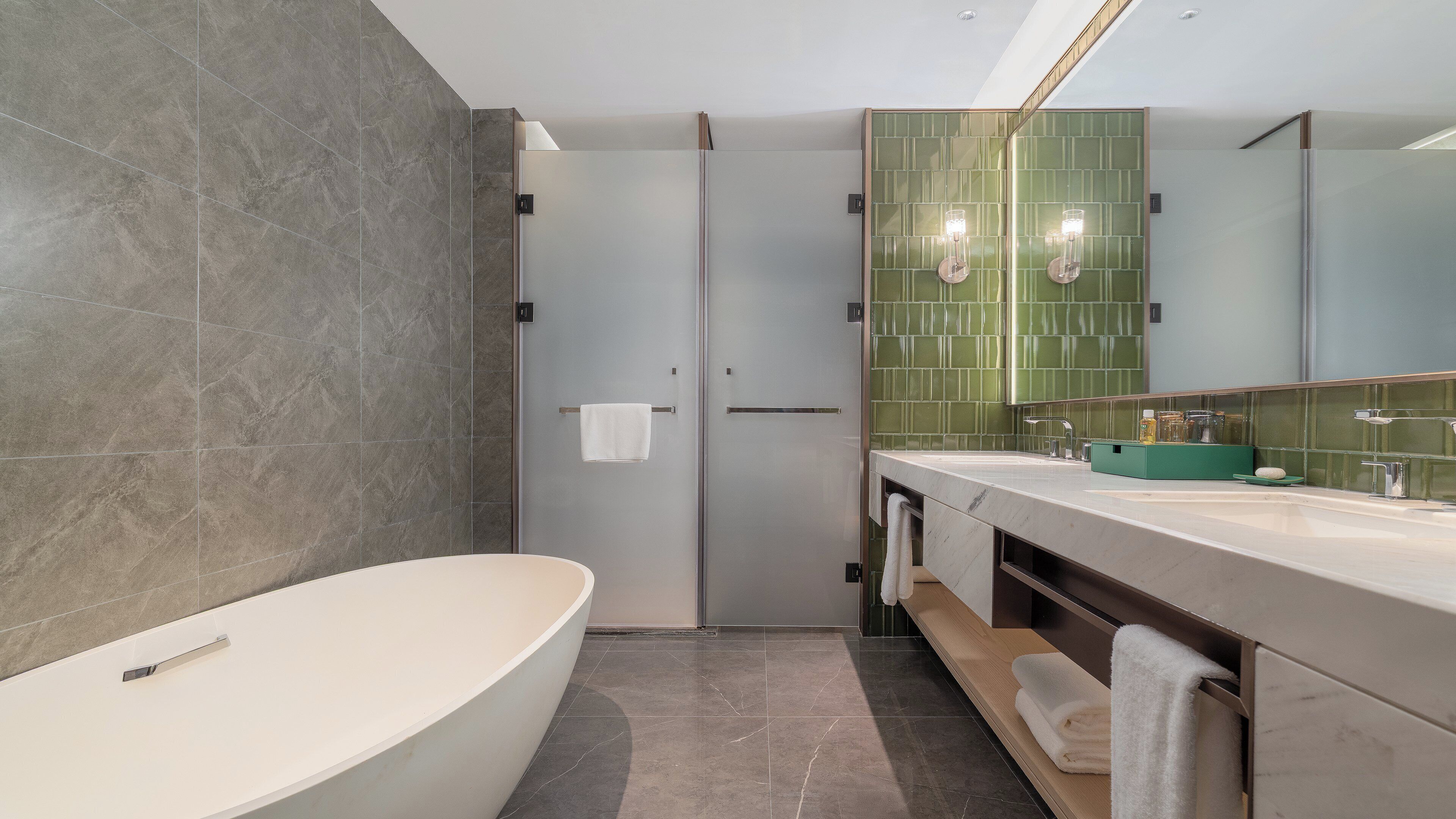 A modern bathroom with a freestanding bathtub, a vanity with a green sink, and a large mirror.