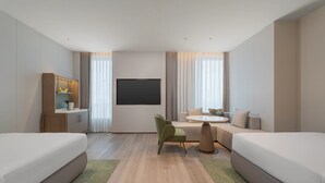 Een hotelkamer met twee bedden, een kleine tafel, een bank, een televisie en een minibar.