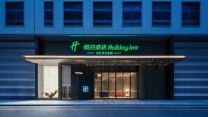 Entree van een Holiday Inn hotel met een modern design, herkenbaar aan een opvallend groen bord en een goed verlichte gevel.