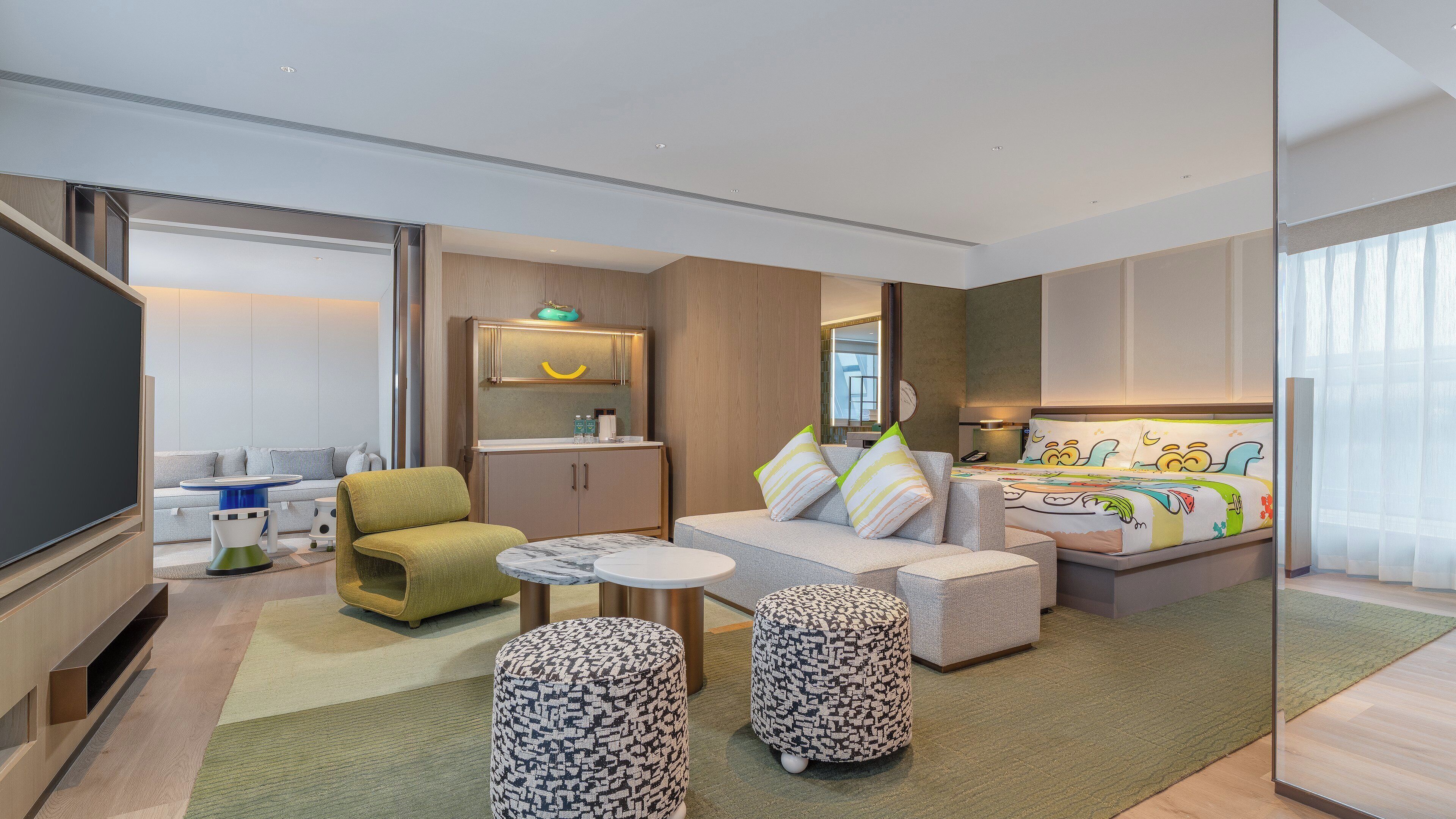 Una habitación de hotel moderna con sofá, cama con ropa de cama colorida, una mesita y un armario.