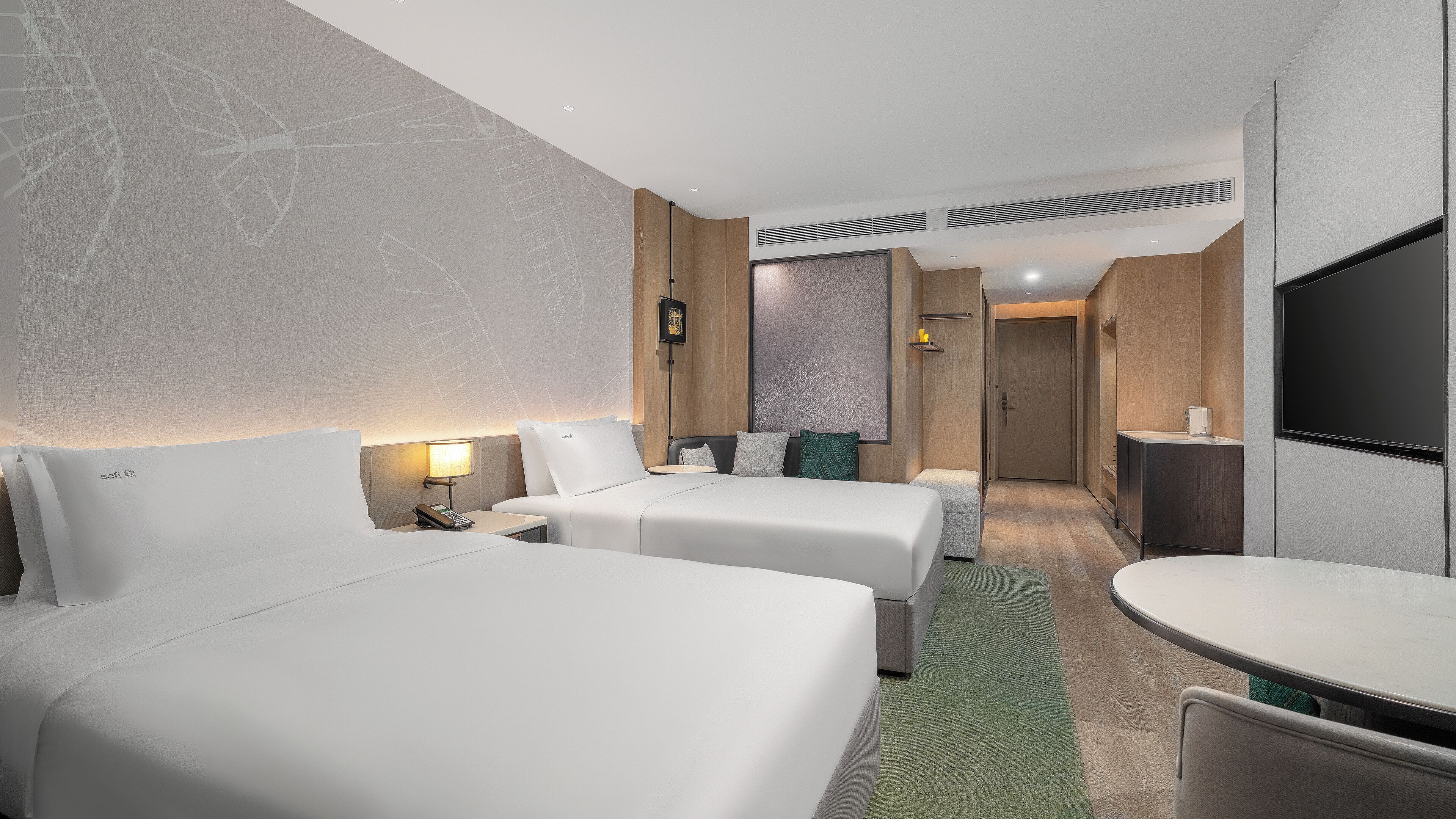 A hotel room with two beds, a desk, a TV, and a bathroom door.