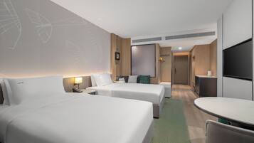A hotel room with two beds, a desk, a TV, and a bathroom door.