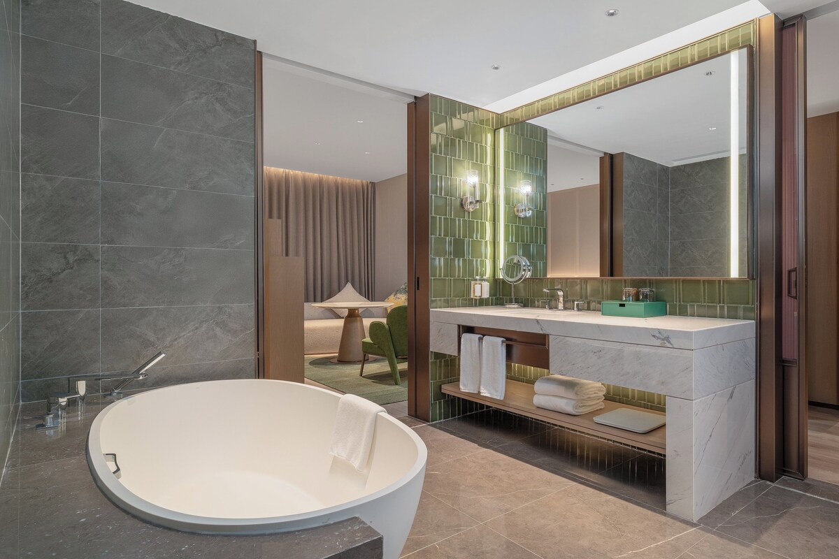 Un baño moderno con una bañera independiente, un espejo grande y un mueble de tocador con un jabonera verde.
