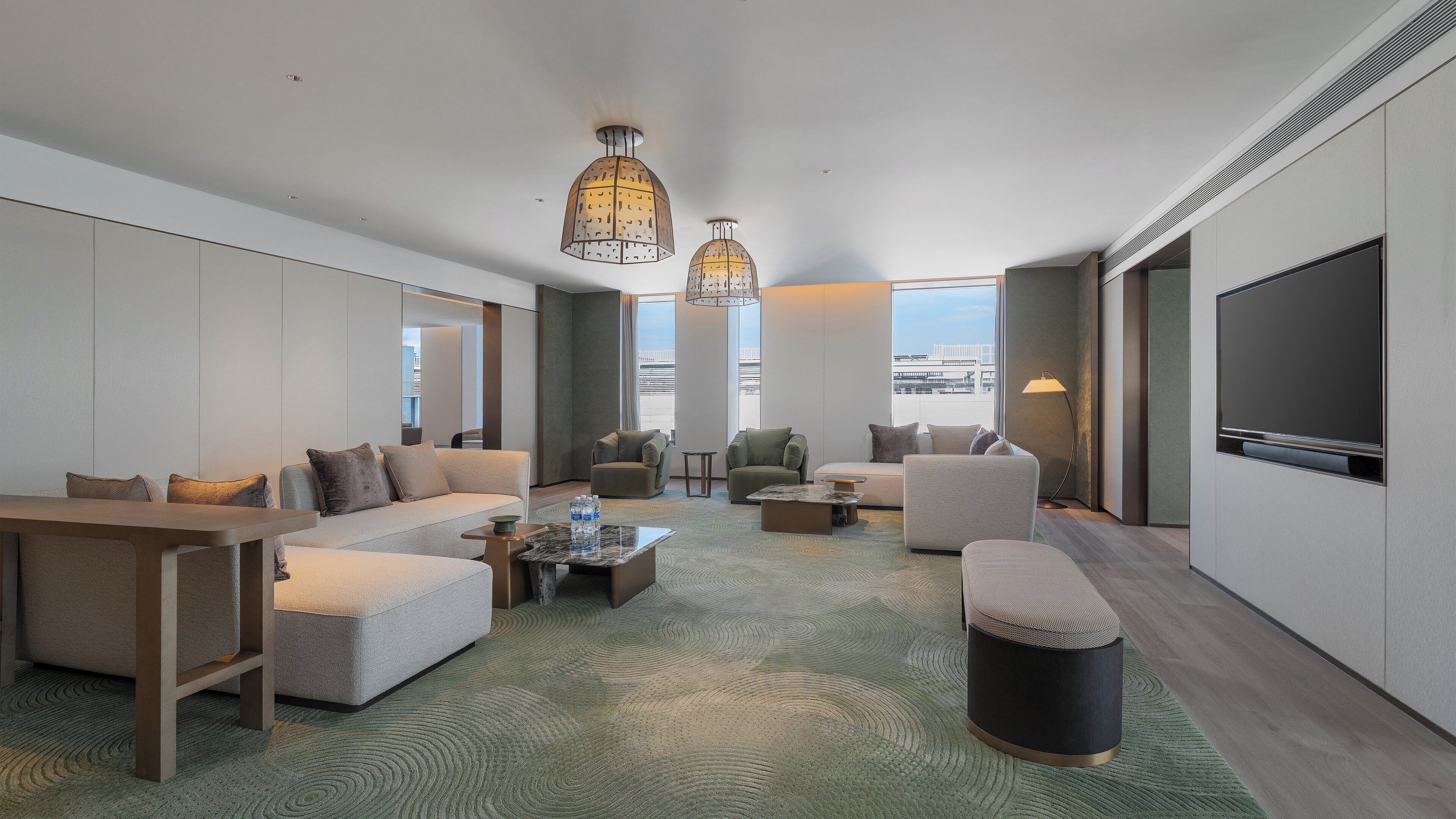 Une chambre d’hôtel moderne comprenant un canapé, des fauteuils, une table basse et un téléviseur.