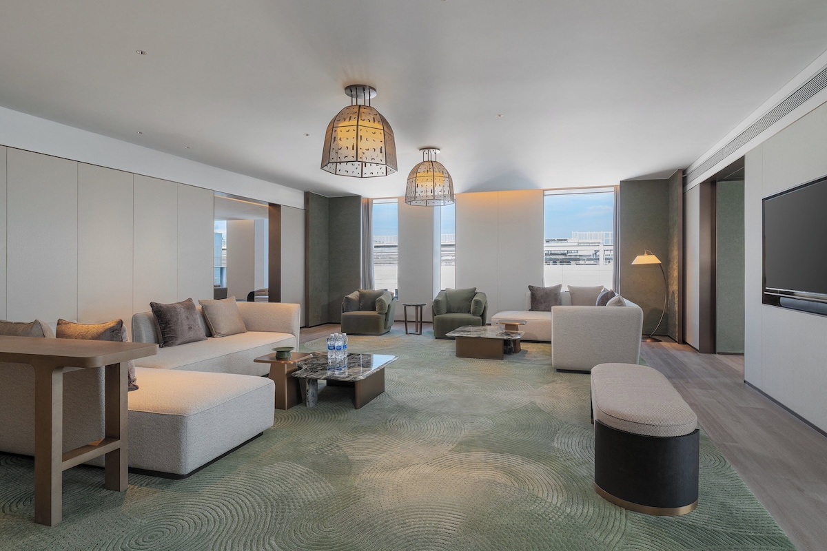 Una habitación de hotel moderna con un conjunto de sofás, sillones, una mesita de centro y un televisor.