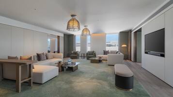 Una habitación de hotel moderna con un conjunto de sofás, sillones, una mesita de centro y un televisor.