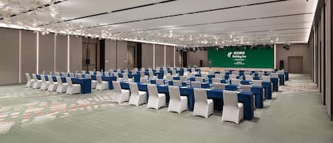 Une salle de conférence avec des rangées de tables et de chaises, un écran vert affichant du texte et une moquette à motifs.