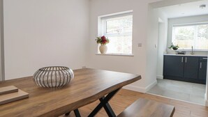 A modern kitchen with dark cabinets, a wooden dining table, and a window with blinds. - 5 Marsh Lane (Flint)