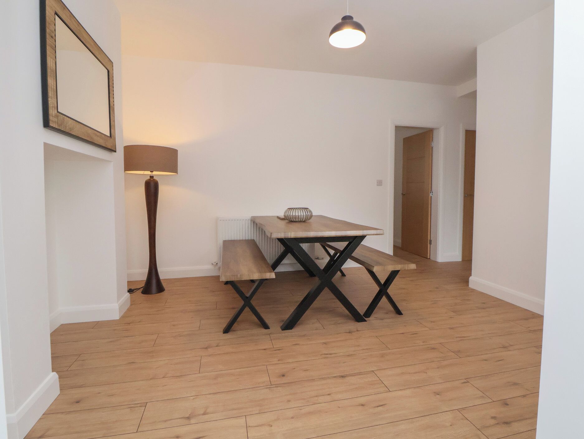 Ein Zimmer mit Holzboden, einem Tisch mit Bänken, einer Lampe und einem gerahmten Bild an der Wand.