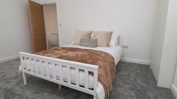 Un dormitorio con una cama blanca, un edredón marrón y dos almohadas.