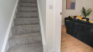 A staircase with carpeted steps leading to a room with a dark-colored sofa and a plant. - 5 Marsh Lane (Flint)