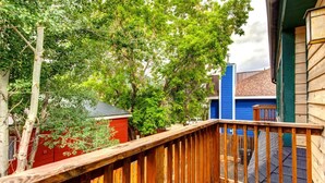 Un pontile in legno con ringhiera, circondato da alberi e un edificio rosso.