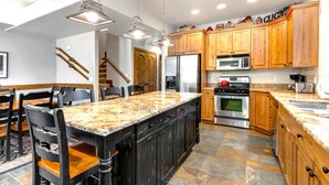 Cucina con mobili in legno, piani di lavoro in granito, isola centrale ed elettrodomestici moderni.