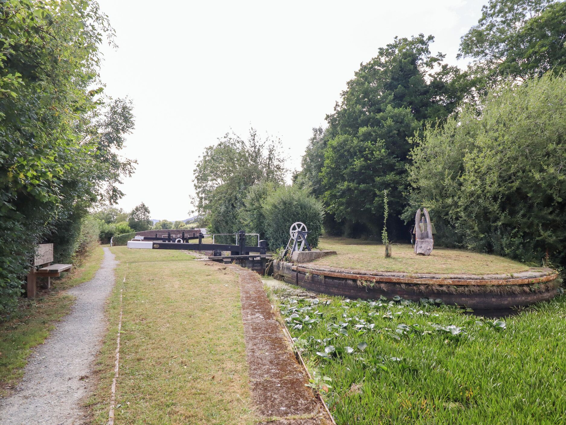 Ein Weg, der zu einem kleinen Teich mit einer Pumpe und einer Statue führt.