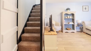 A staircase leading to a living room with a television, a cabinet, and a sofa. - Lockmans Cottage (Llanymynech)