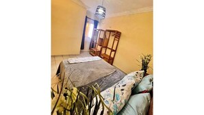 A bedroom with a bed, a wooden wardrobe, a small table, and a potted plant. - Residence Ethan Nji - Amazing loft (Yaoundé)