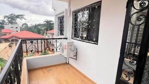 A balcony with a wooden floor, a black metal railing, a black door with decorative patterns, and a wall-mounted light fixture. - Residence Ethan Nji - Amazing loft (Yaoundé)