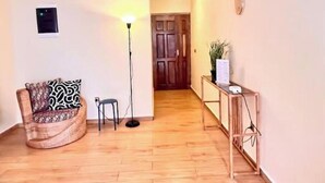 A room with a wooden floor, a patterned sofa, a standing lamp, a small table with a plant, and a door in the background. - Residence Ethan Nji - Amazing loft (Yaoundé)