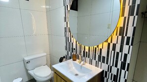A bathroom with a white toilet, a sink with a mirror above it, and a tiled wall with a black and white checkered pattern. - Luxury Apartment: 3BR\2BA\6G Work, Studio & Family - Live Like a Local Peruvian (Lima)