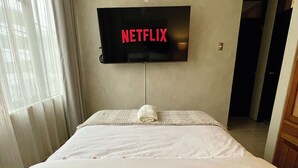 A hotel room with a bed, a TV mounted on the wall displaying 'NETFLIX', and a window with curtains. - Luxury Apartment: 3BR\2BA\6G Work, Studio & Family - Live Like a Local Peruvian (Lima)