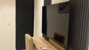 A modern living room with a wooden dining table, a beige sofa, a flat-screen TV, and a black door. - Adar Hotel (Lagos)