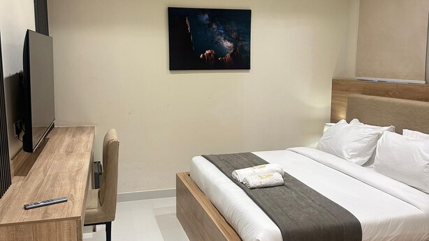 A modern hotel room with a wooden bed, a desk, and a mounted TV. - Adar Hotel (Lagos)