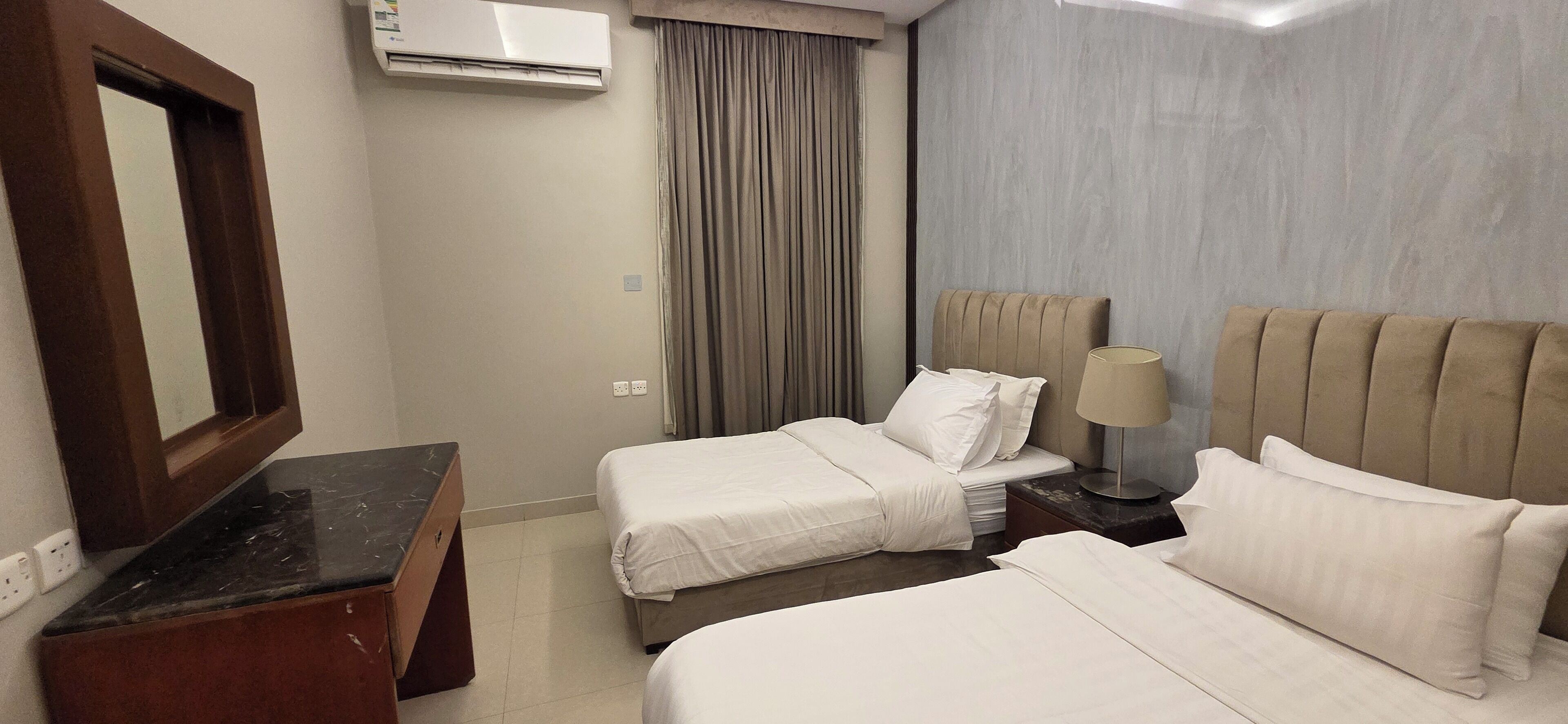 Une chambre d’hôtel avec deux lits, un bureau, un climatiseur, une lampe et une fenêtre avec des rideaux.
