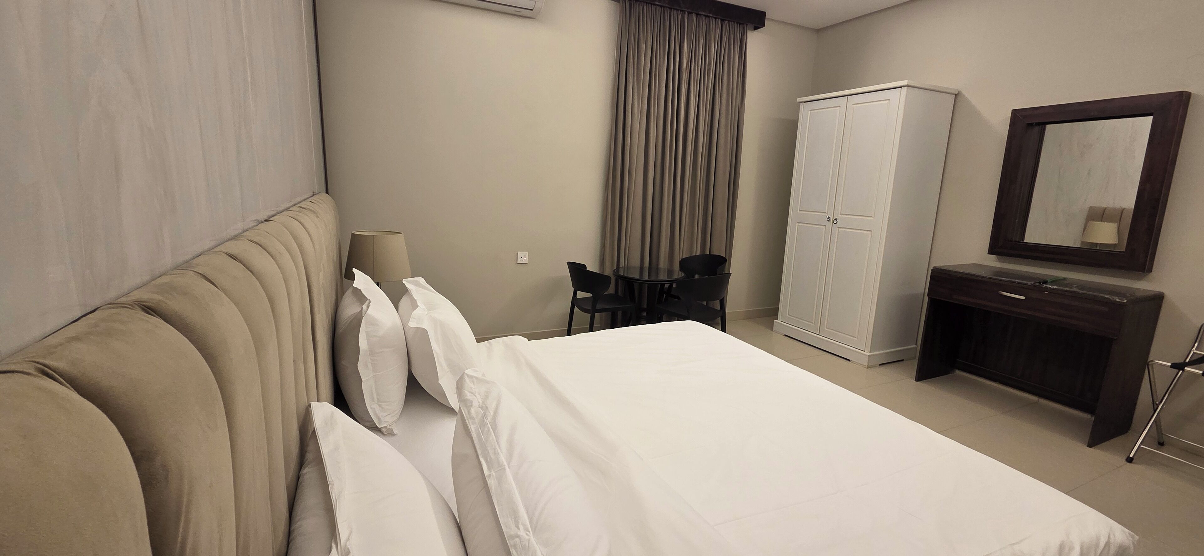 A hotel room with a bed, a desk, a chair, a wardrobe, and a mirror.