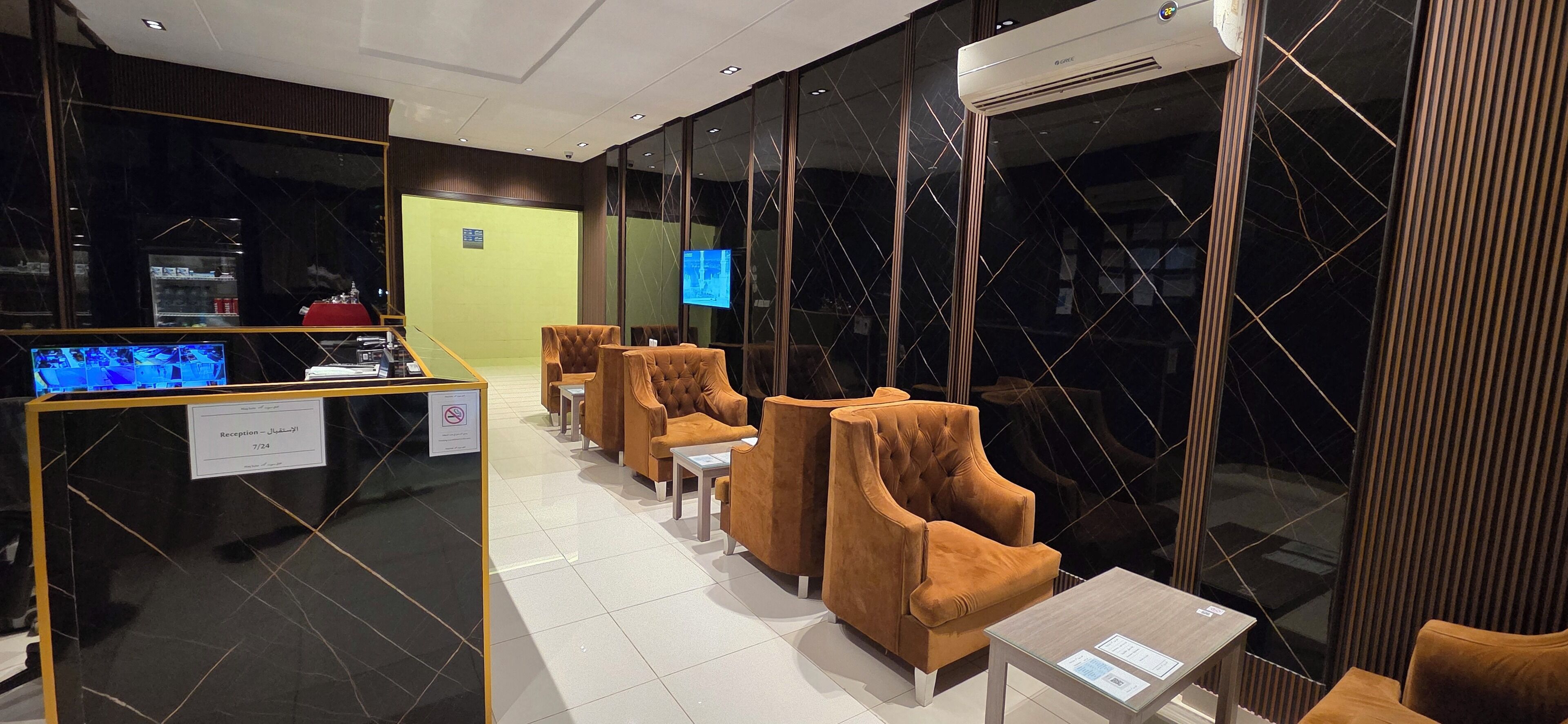 Un área de recepción con mostrador, televisor y asientos con mesas.