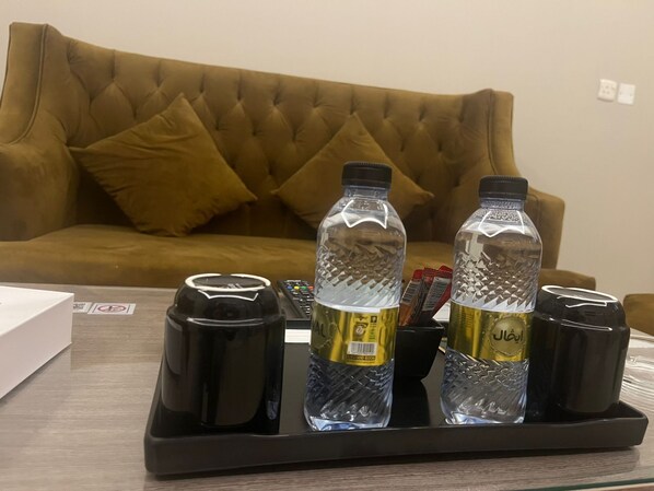 A tray with two water bottles, a black container, and a remote control on a table in front of a brown sofa.