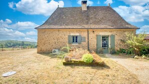 A rustic stone house with a sloped roof, a chimney, and a small garden with potted plants and a bush. - Charmante Maison avec piscine (Journiac)