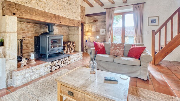 A cozy living room with a stone fireplace, a sofa, and a wooden coffee table. - Charmante Maison avec piscine (Journiac)