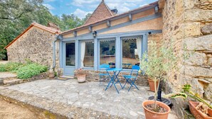 A stone building with a tiled roof, a covered patio with blue chairs, and potted plants. - Charmante Maison avec piscine (Journiac)