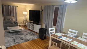 A living room with a sofa, TV, and a dining area with a table and chairs. - Charming 3-bedroom house in delightful Peabody (Peabody)