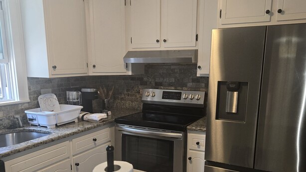 A modern kitchen with white cabinets, a stainless steel refrigerator, an oven, and a countertop with a paper towel holder. - Charming 3-bedroom house in delightful Peabody (Peabody)