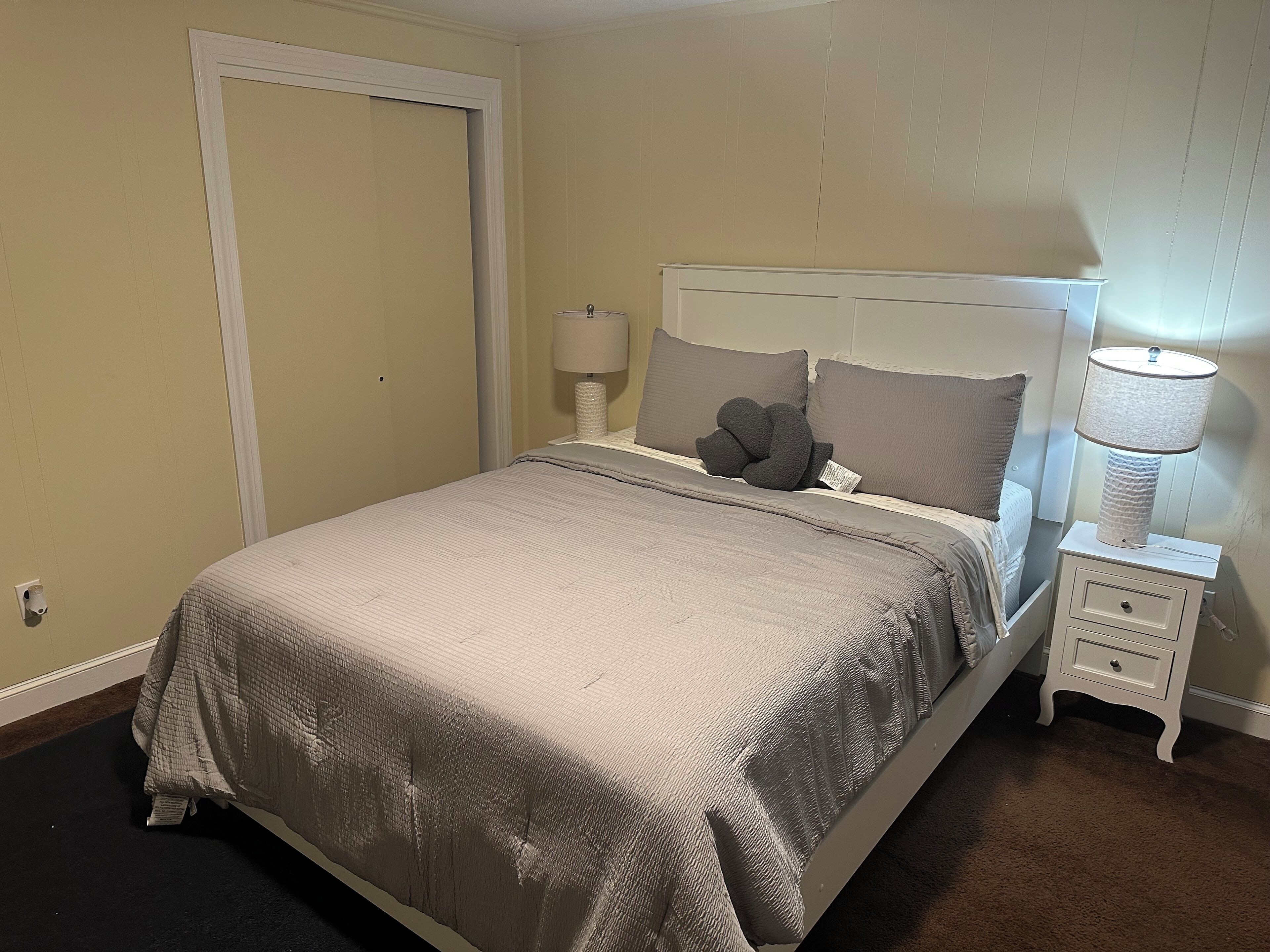 Een netjes opgemaakt bed met hoofdbord, bedlampje en nachtkastje met een lade.